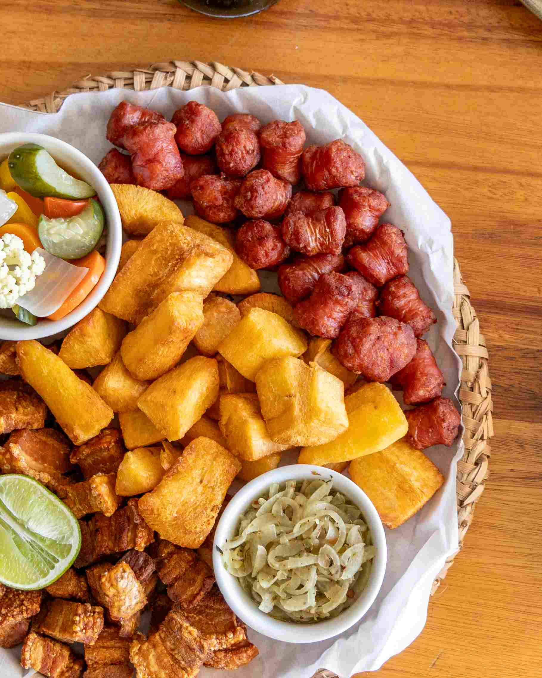 Bar do Geraldinho – Um encontro irresistível de sabores brasileiros: torresmo crocante, aipim macio e dourado, linguicinha suculenta de porco e o toque agridoce dos picles para equilibrar. Acompanha molho de cebola. - Foto: Olho Gordo